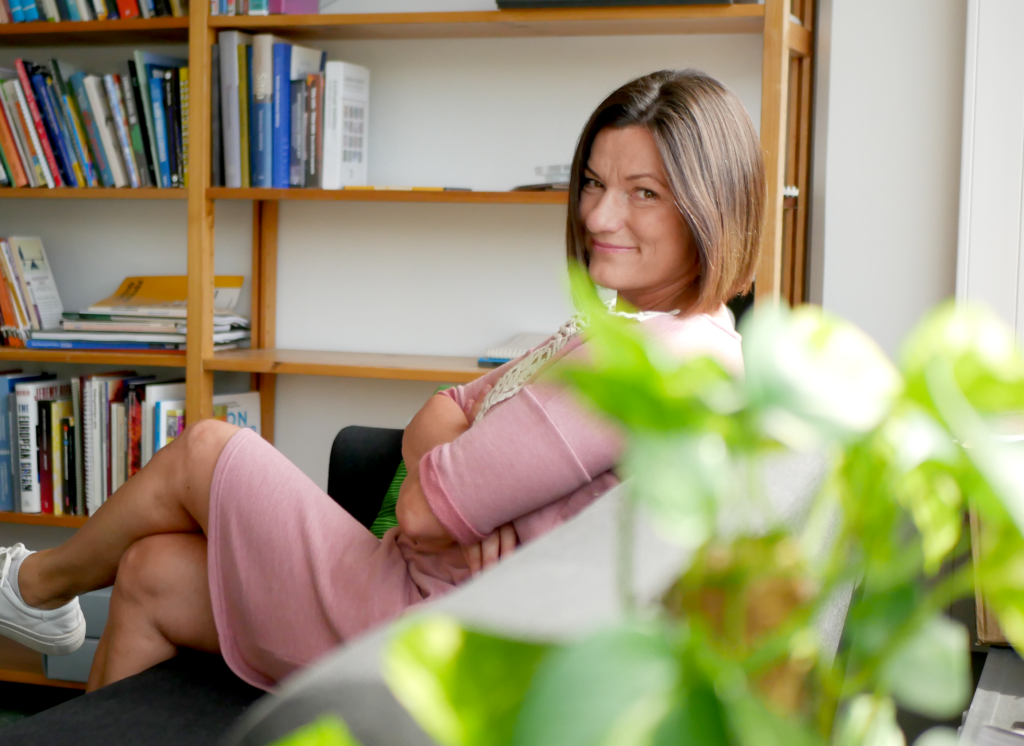 Katja Alvoittu istuu vaaleanpunaisessa mekossa sohvalla Vision kirjastossa.